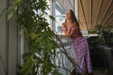 Photo of Beautiful young woman with long hair standing on balcony