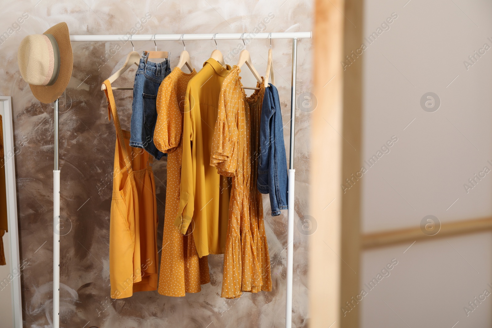 Photo of Different stylish clothes hanging on rack in room