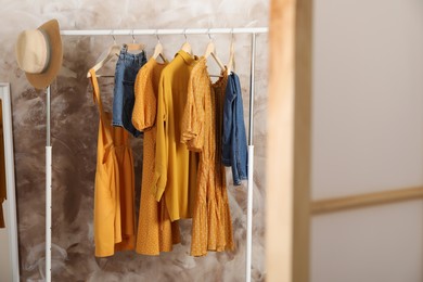 Different stylish clothes hanging on rack in room