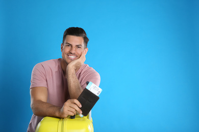 Happy man with suitcase and ticket in passport for summer trip on blue background. Vacation travel