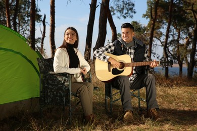 Couple with guitar resting in camping chairs near tent outdoors