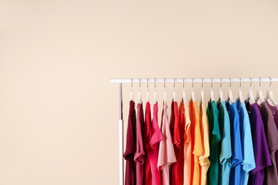 Photo of Many t-shirts hanging in order of rainbow colors on light background