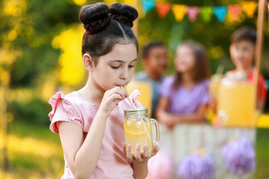 Photo of Cute little girl drinking natural lemonade in park, space for text. Summer refreshing beverage