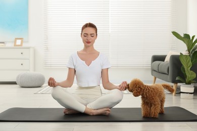 Young woman practicing yoga on mat with her cute dog at home