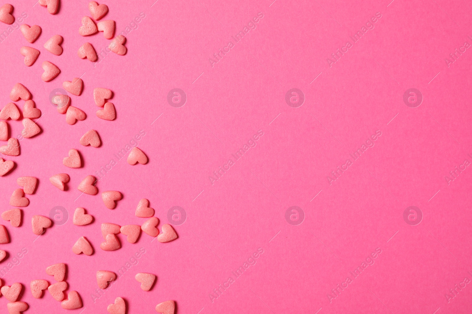 Photo of Heart shaped sprinkles on pink background, flat lay. Space for text