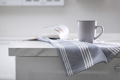 Photo of Kitchen towel, cup and magazine on white marble table