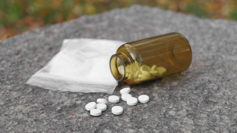 Plastic bag with powder and pills on stone surface outdoors, closeup. Hard drugs