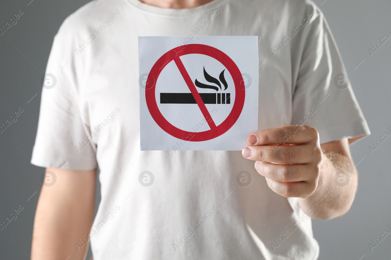 Photo of Man holding card with no smoking sign on gray background, closeup