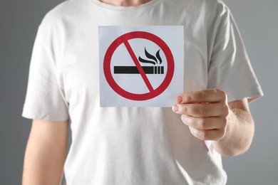 Man holding card with no smoking sign on gray background, closeup