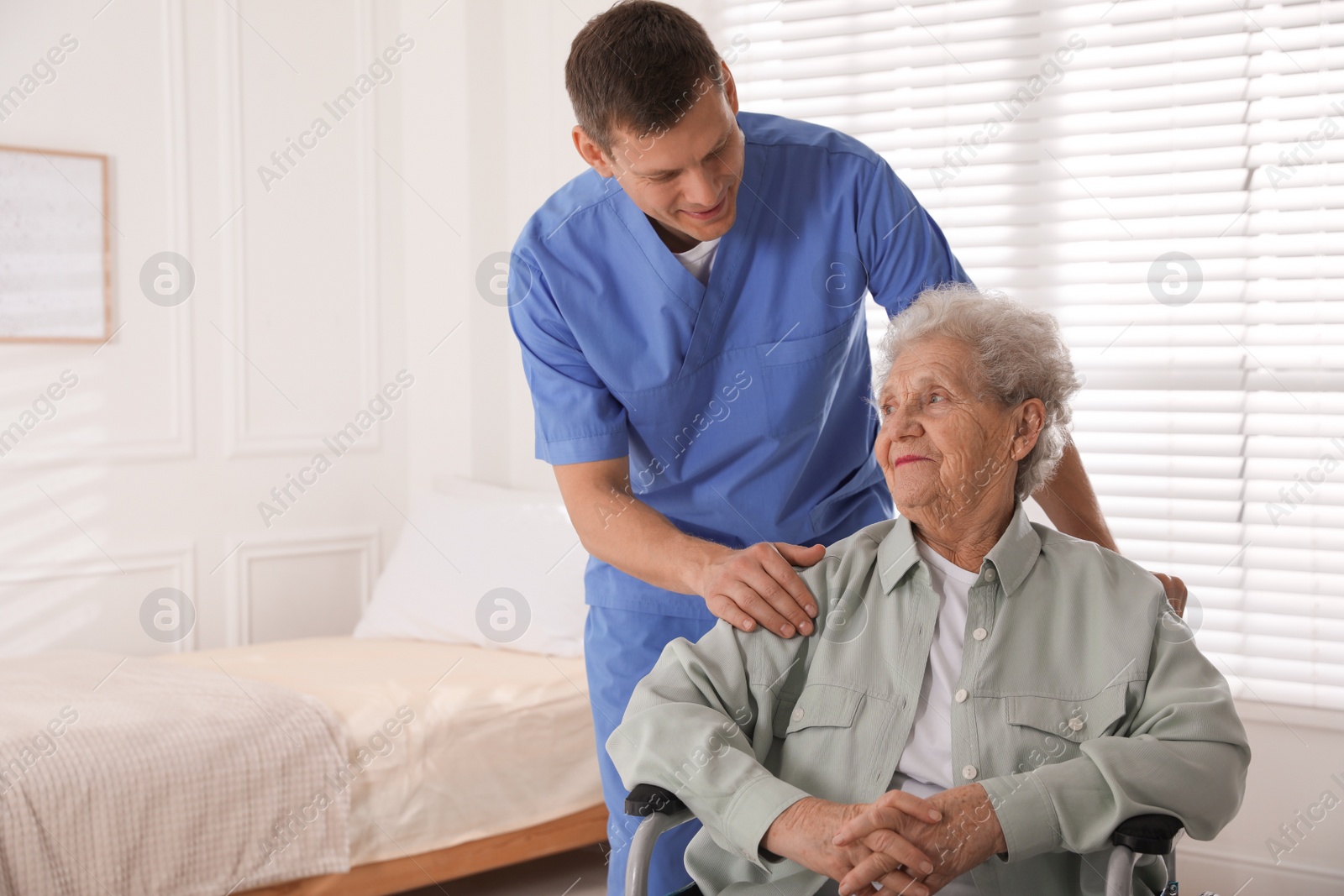 Photo of Caregiver assisting senior woman in wheelchair indoors. Home health care service