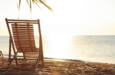 Photo of Wooden deck chair on sandy beach. Summer vacation