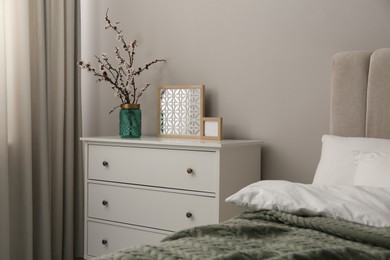 Photo of Flowering tree twigs and decor on white chest of drawers in bedroom
