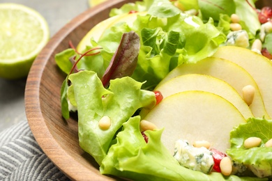 Fresh salad with pear slices in wooden bowl, closeup