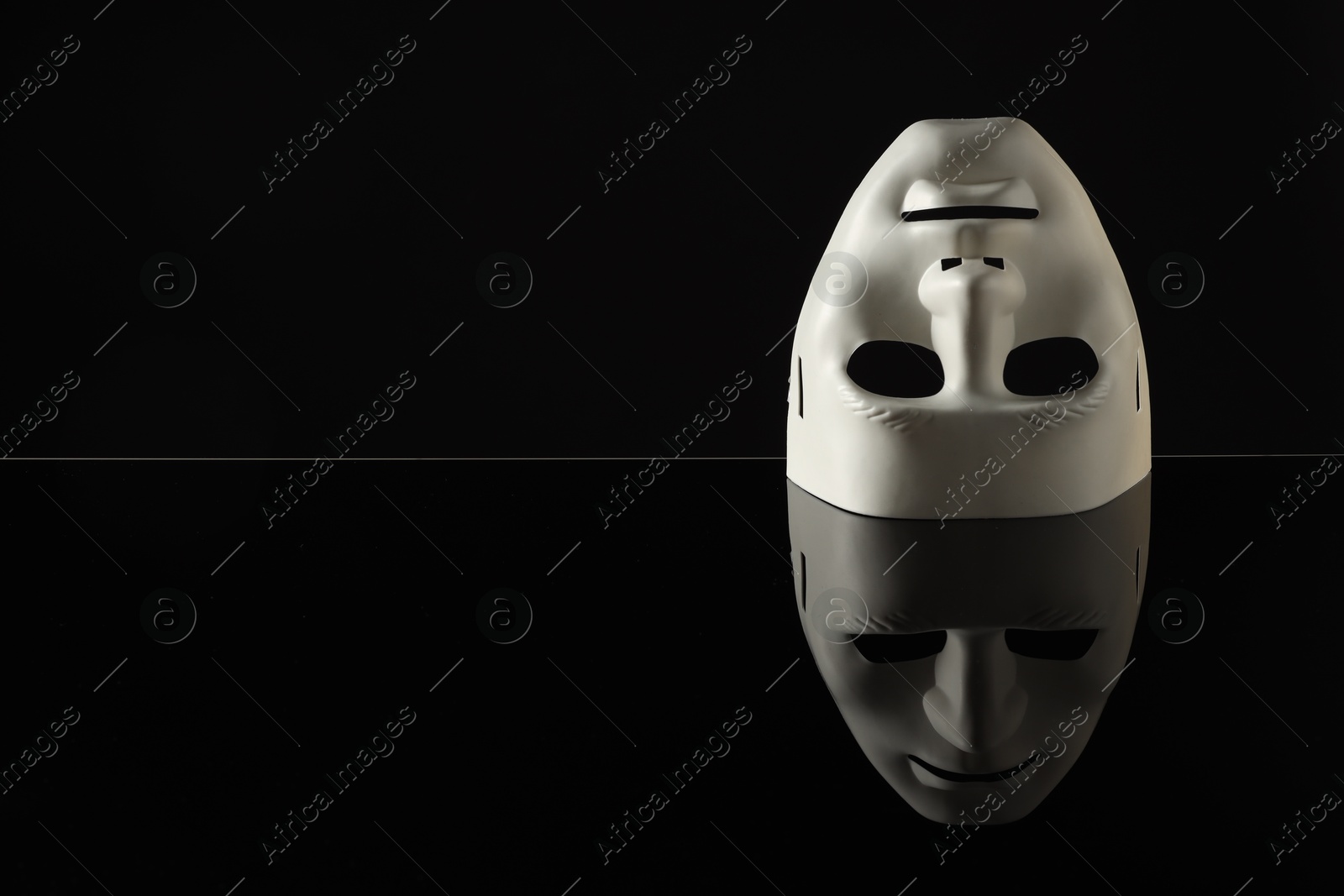 Photo of Plastic face mask on black mirror surface, space for text. Theatrical performance
