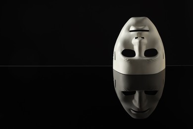 Photo of Plastic face mask on black mirror surface, space for text. Theatrical performance