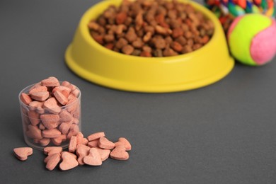 Photo of Vitamins, toys and dry pet food in bowl on grey background, space for text
