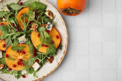 Tasty salad with persimmon, blue cheese, pomegranate and walnuts served on white tiled table, top view. Space for text