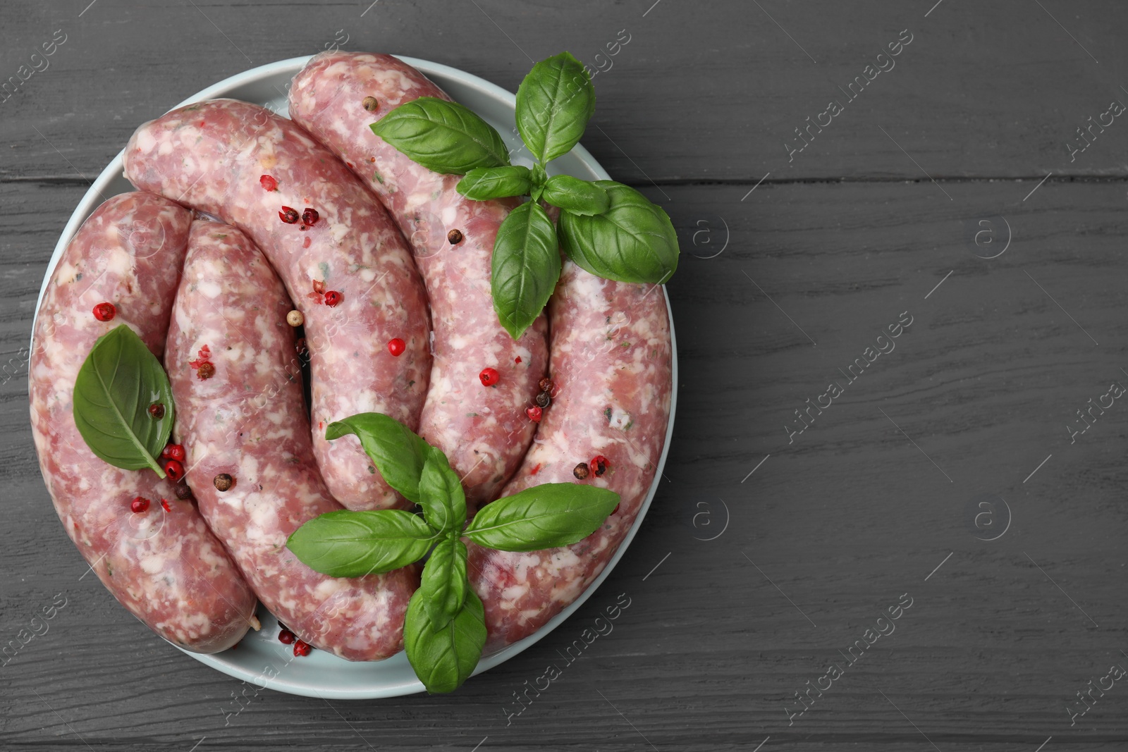 Photo of Raw homemade sausages, basil leaves and peppercorns on grey wooden table, top view. Space for text