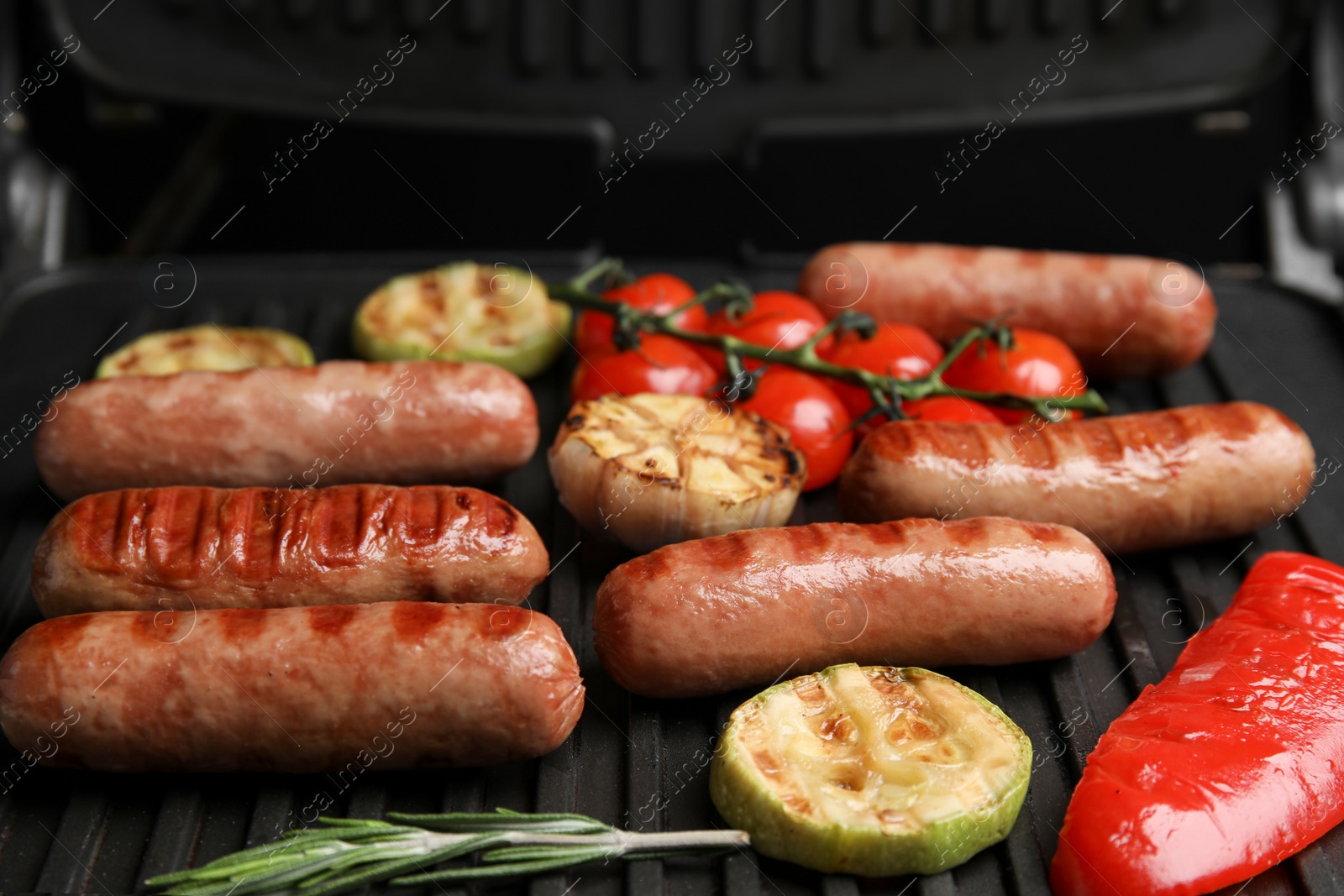 Photo of Cooking delicious fresh sausages with vegetables on modern grill