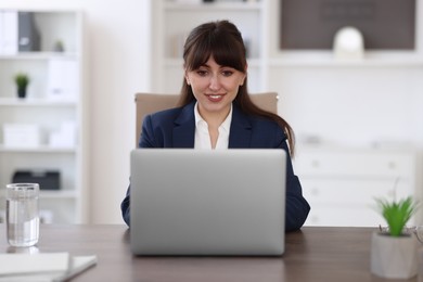 Photo of Woman watching webinar at wooden table in office
