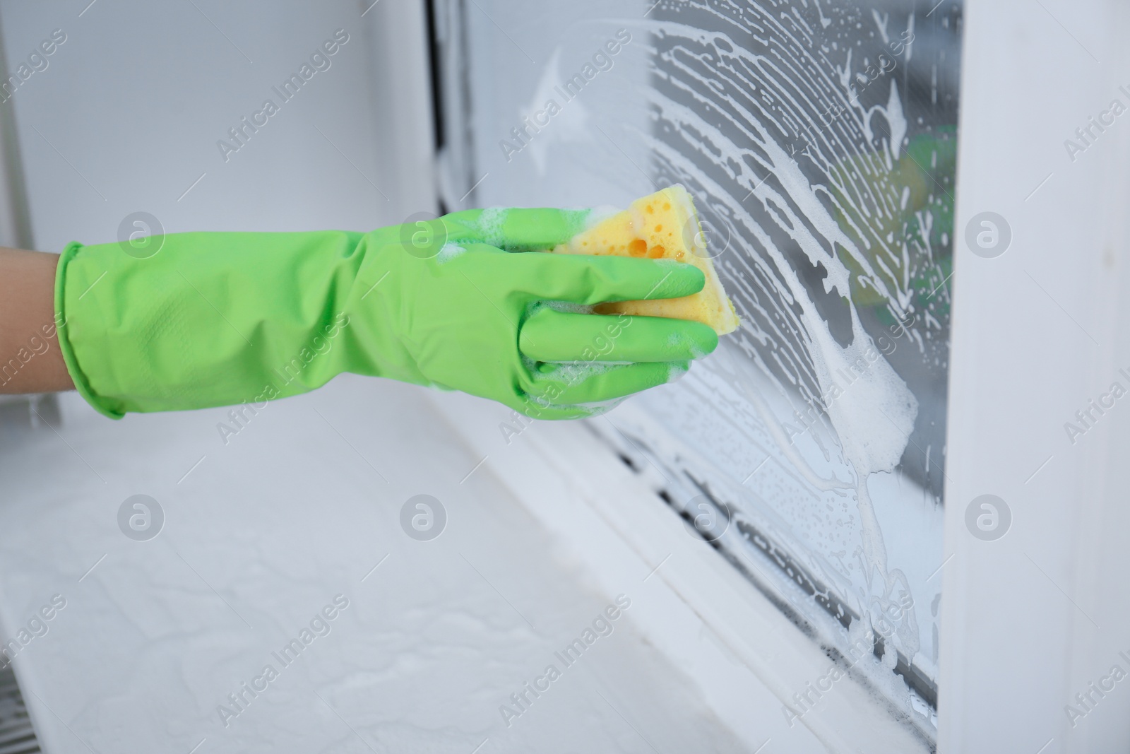 Photo of Woman cleaning window with sponge indoors, closeup