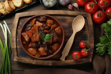 Photo of Delicious beef stew with carrots, parsley and potatoes on wooden table, flat lay