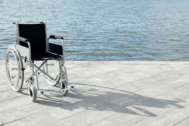 Photo of Empty wheelchair near river on sunny day. Space for text