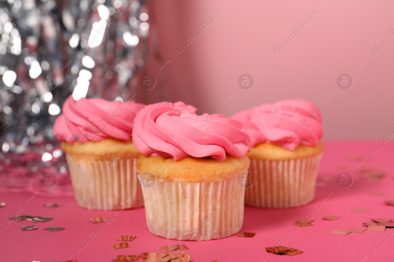 Photo of Delicious cupcakes with bright cream and confetti on pink table, closeup