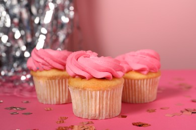 Photo of Delicious cupcakes with bright cream and confetti on pink table, closeup