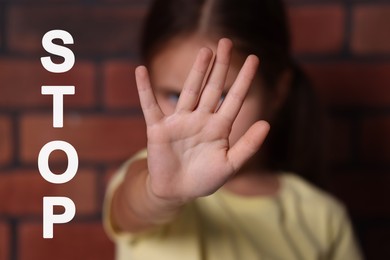 Image of No child abuse. Little girl making stop gesture near brick wall, selective focus