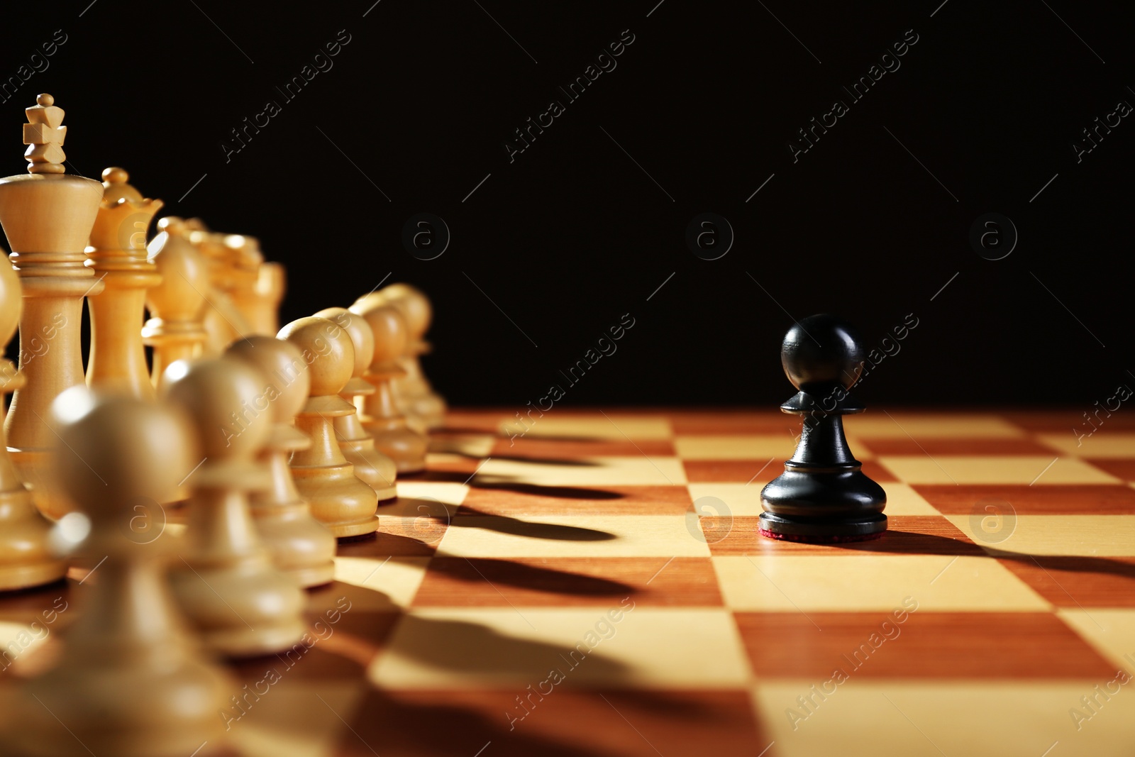 Photo of Black pawn in front of white pieces on wooden board against dark background. Competition concept