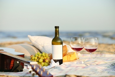 Photo of Blanket with food, wine and guitar on beach. Romantic picnic for couple