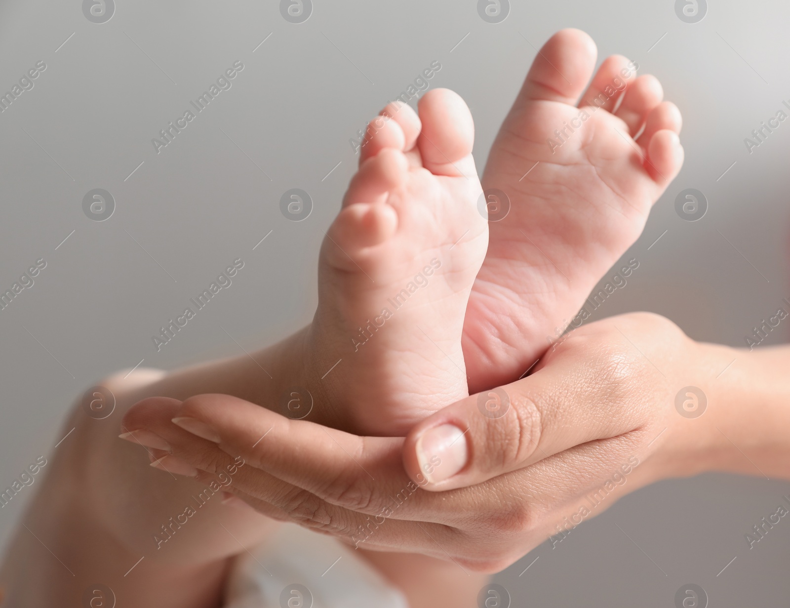 Photo of Mother holding her baby on grey background, closeup on feet