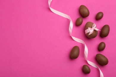 Photo of Sweet chocolate eggs and ribbon on pink background, flat lay. Space for text