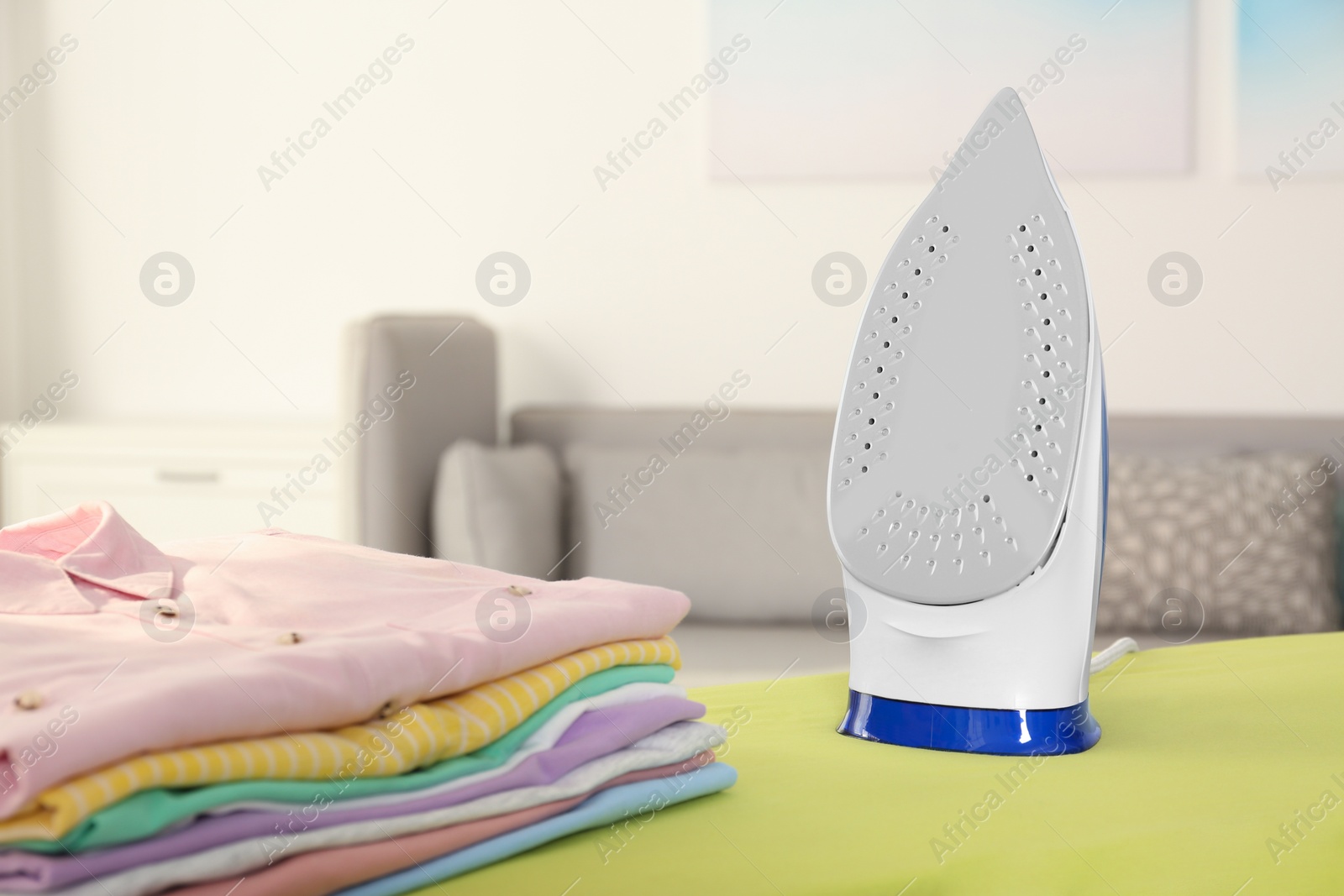 Photo of Board with modern iron and clean laundry at home