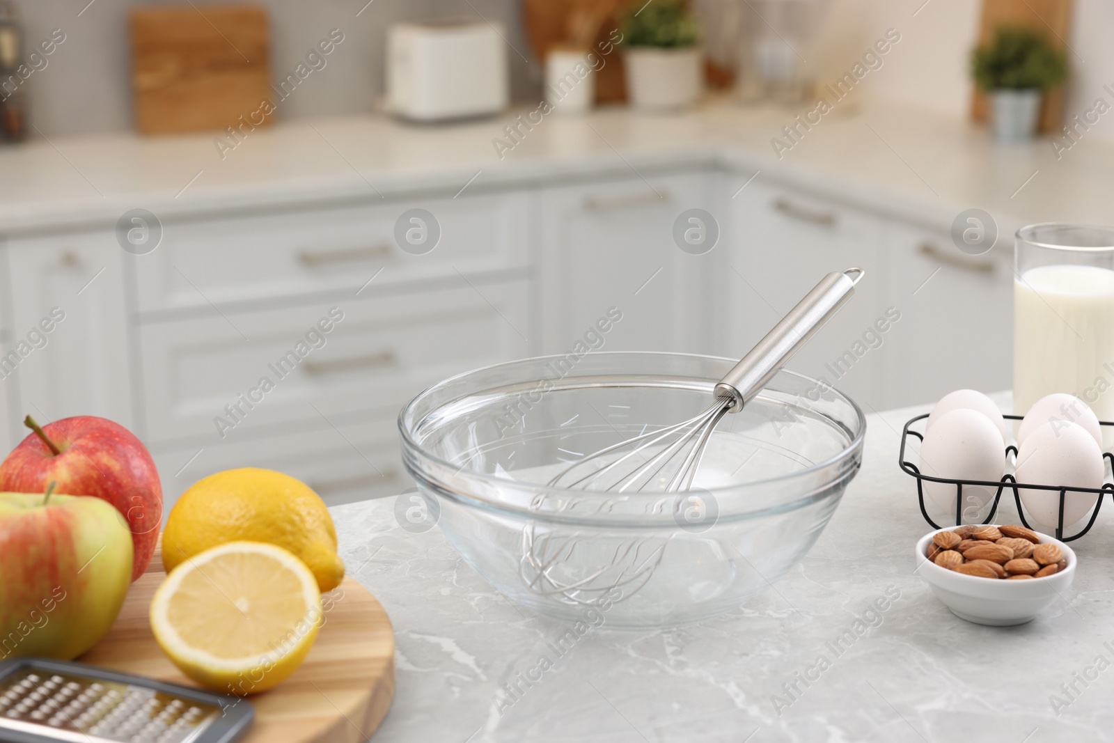 Photo of Metal whisk, bowl, grater and different products on gray marble table in kitchen