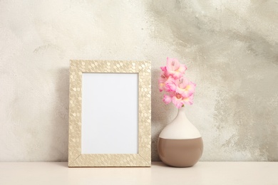 Blank frame and vase with flowers on table near color wall. Mock up for design