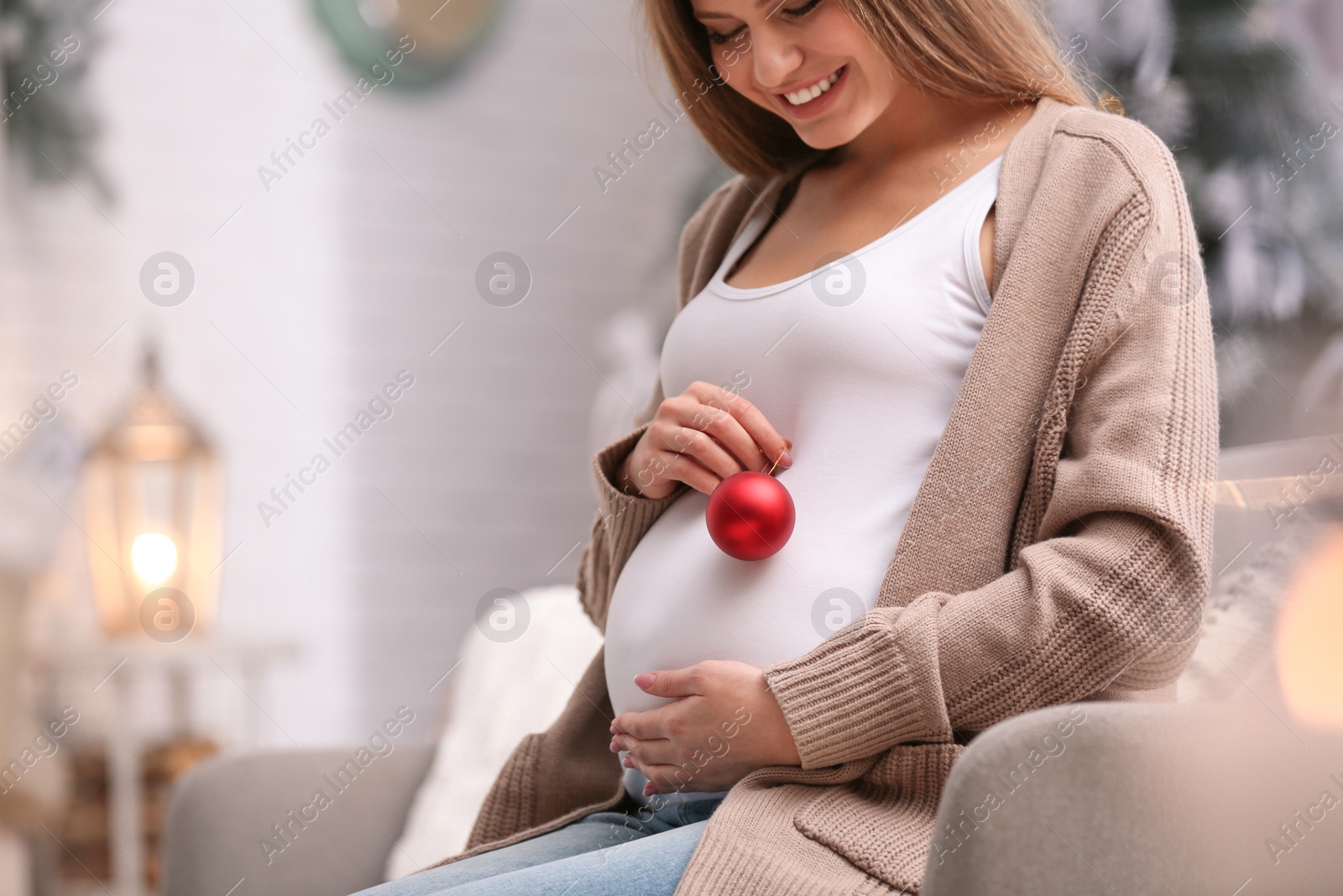 Photo of Young pregnant woman with Christmas decoration at home, closeup