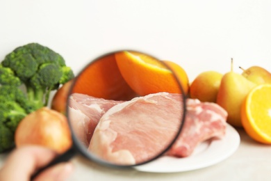 Photo of Woman with magnifying glass exploring raw meat and fruits, closeup. Poison detection