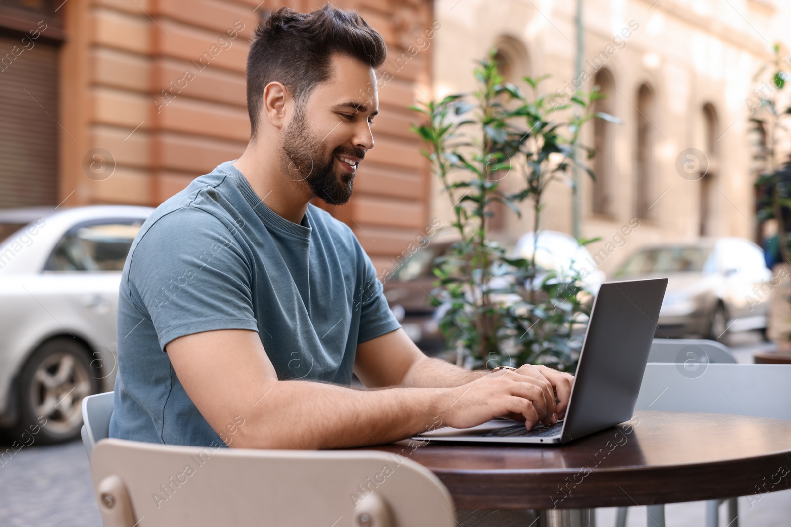 Photo of Handsome young man working on laptop at table in outdoor cafe