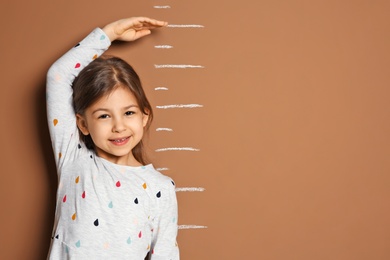 Photo of Little girl measuring her height on color background