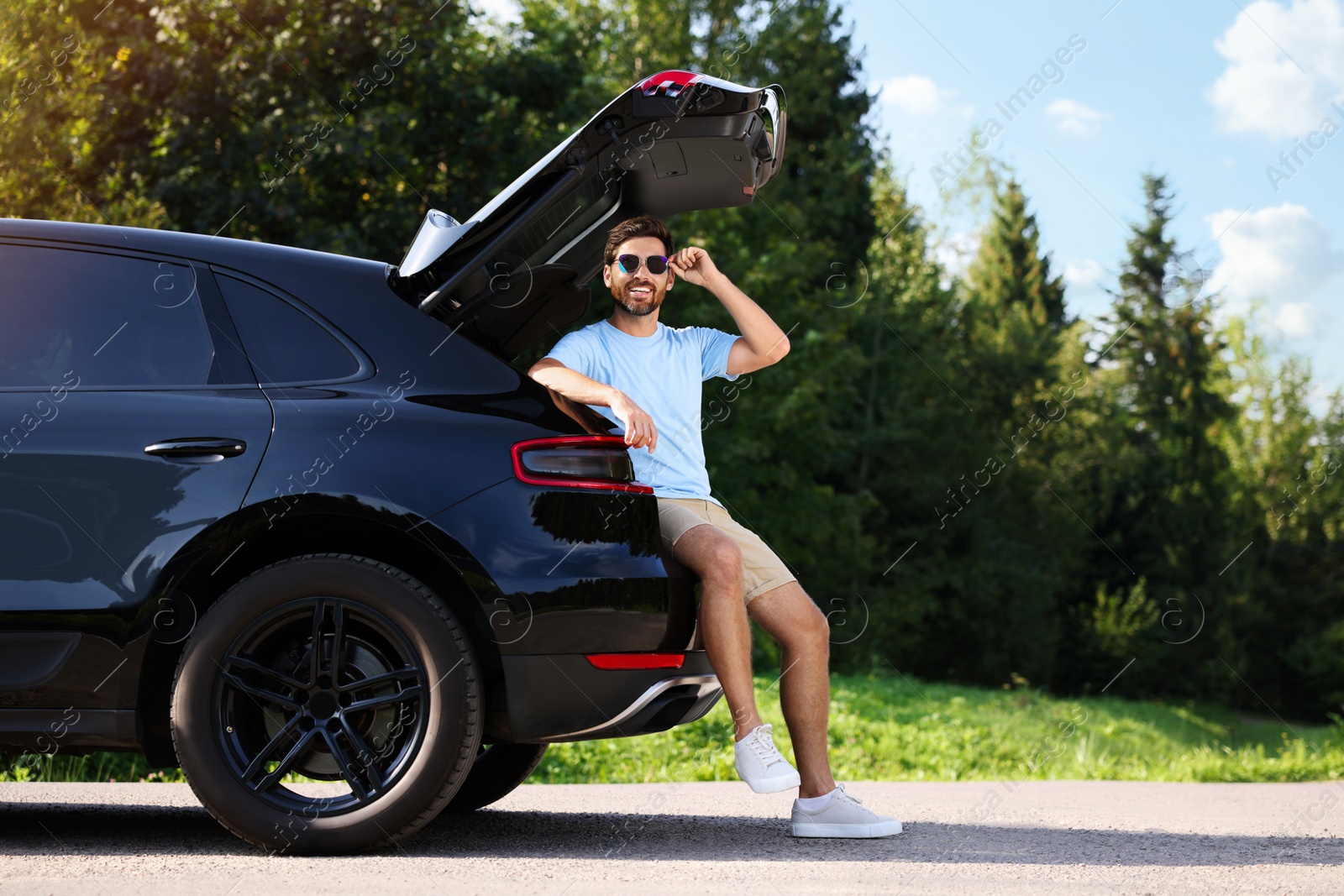 Photo of Happy man sitting in trunk of modern car outdoors