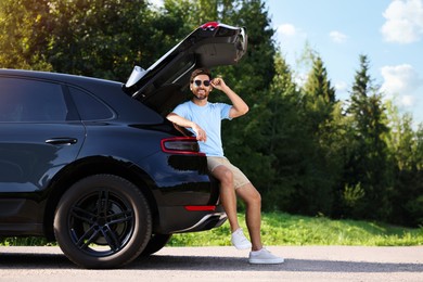 Photo of Happy man sitting in trunk of modern car outdoors
