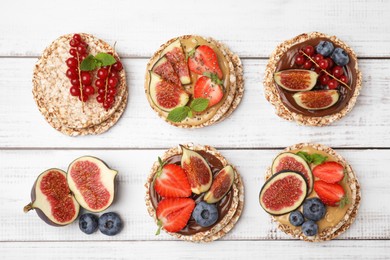 Photo of Tasty crispbreads with different toppings on white wooden table, flat lay