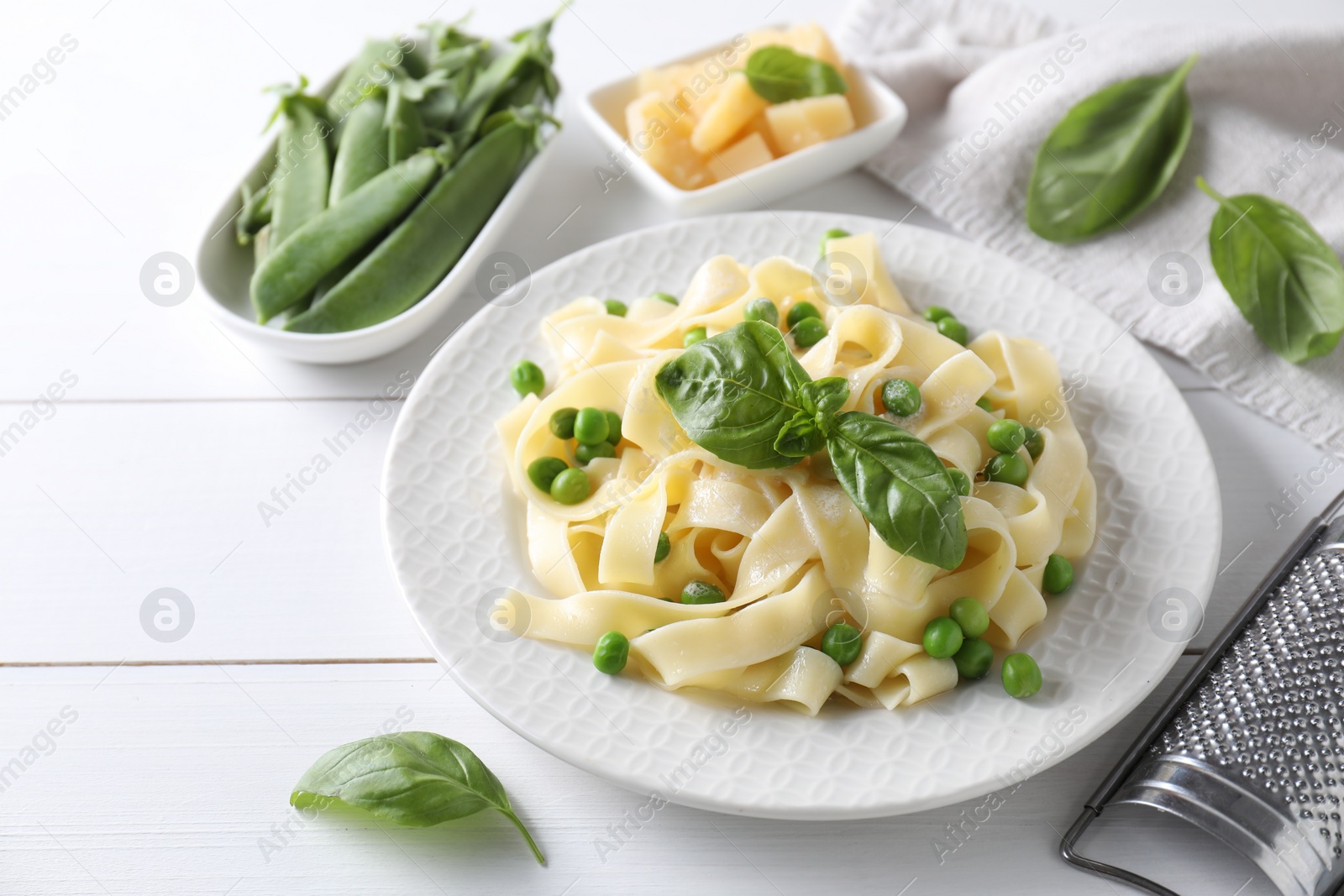 Photo of Delicious pasta with green peas and fresh basil on white wooden table