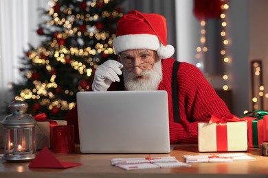 Photo of Emotional Santa Claus using laptop at his workplace in room with Christmas tree