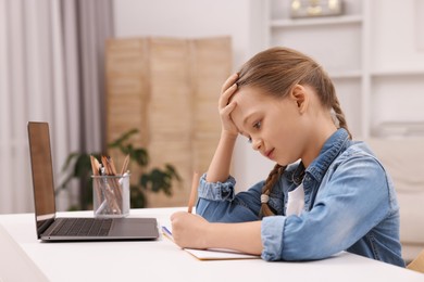 Photo of Little girl suffering from headache while doing homework at home