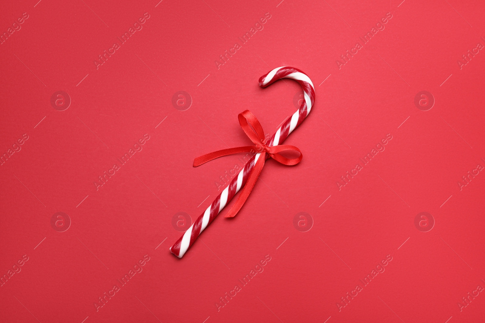 Photo of Sweet Christmas candy cane with bow on red background, top view