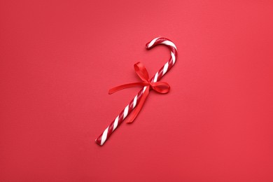 Photo of Sweet Christmas candy cane with bow on red background, top view