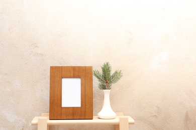 Photo of Blank frame and vase with fir branch on table near color wall. Mock up for design